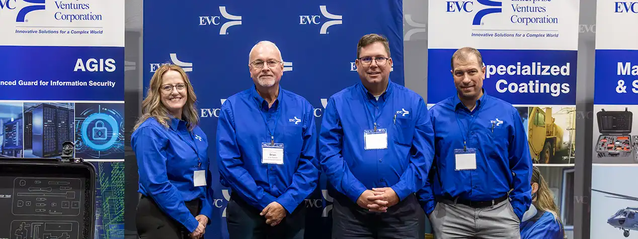 Four EVC employees wearing blue shirts, standing in the EVC booth at a trade show